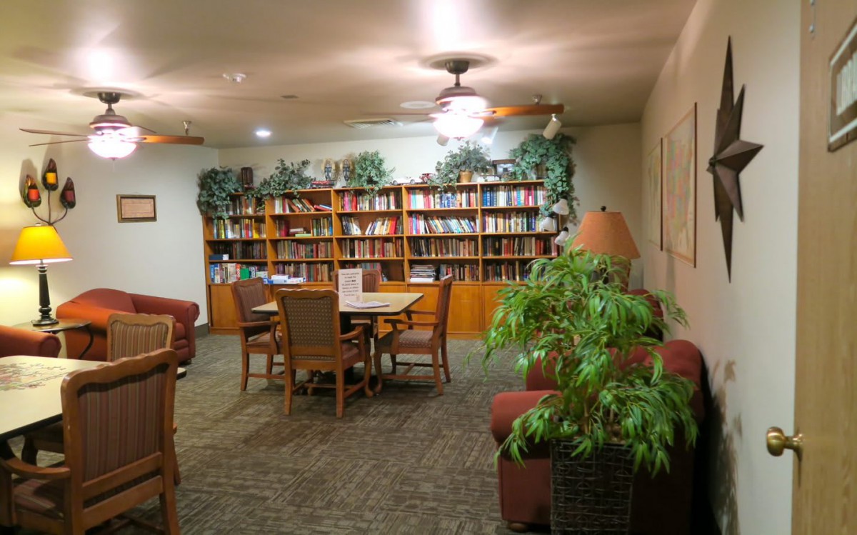 A cozy library space with bookshelves, tables, chairs, and indoor plants.