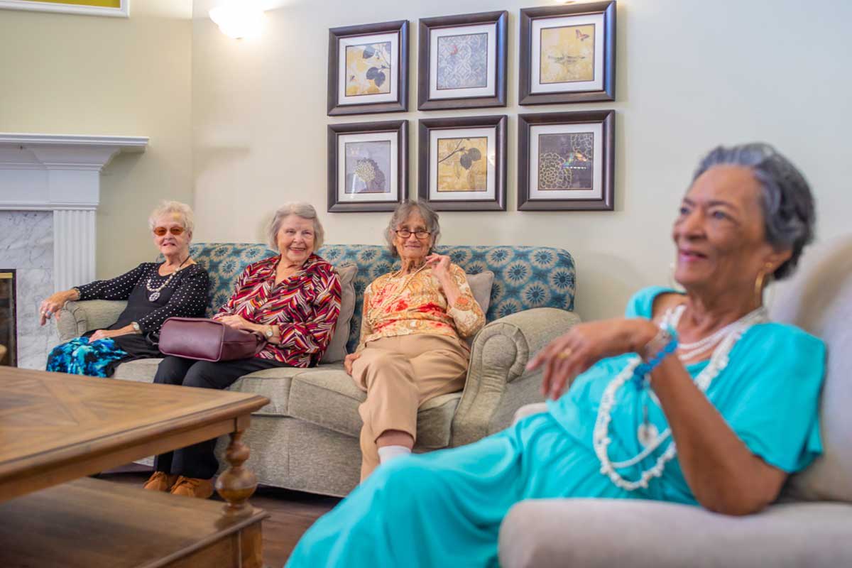 A group of seniors sitting together in a living room, engaging in conversation.
