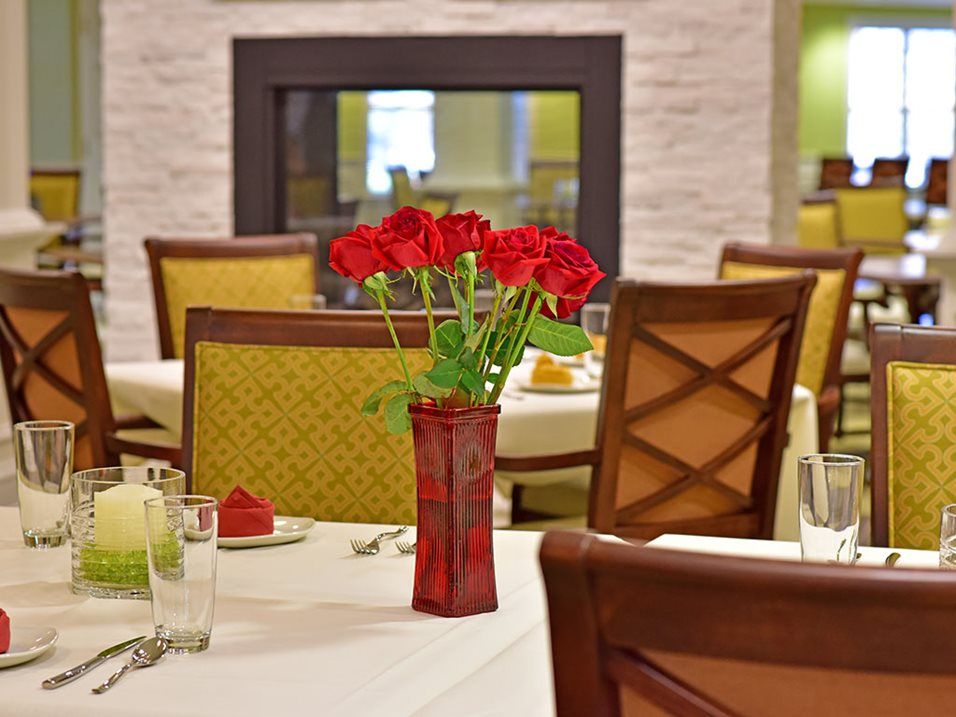 An elegantly set dining table with red roses in a vase, located in a restaurant interior.