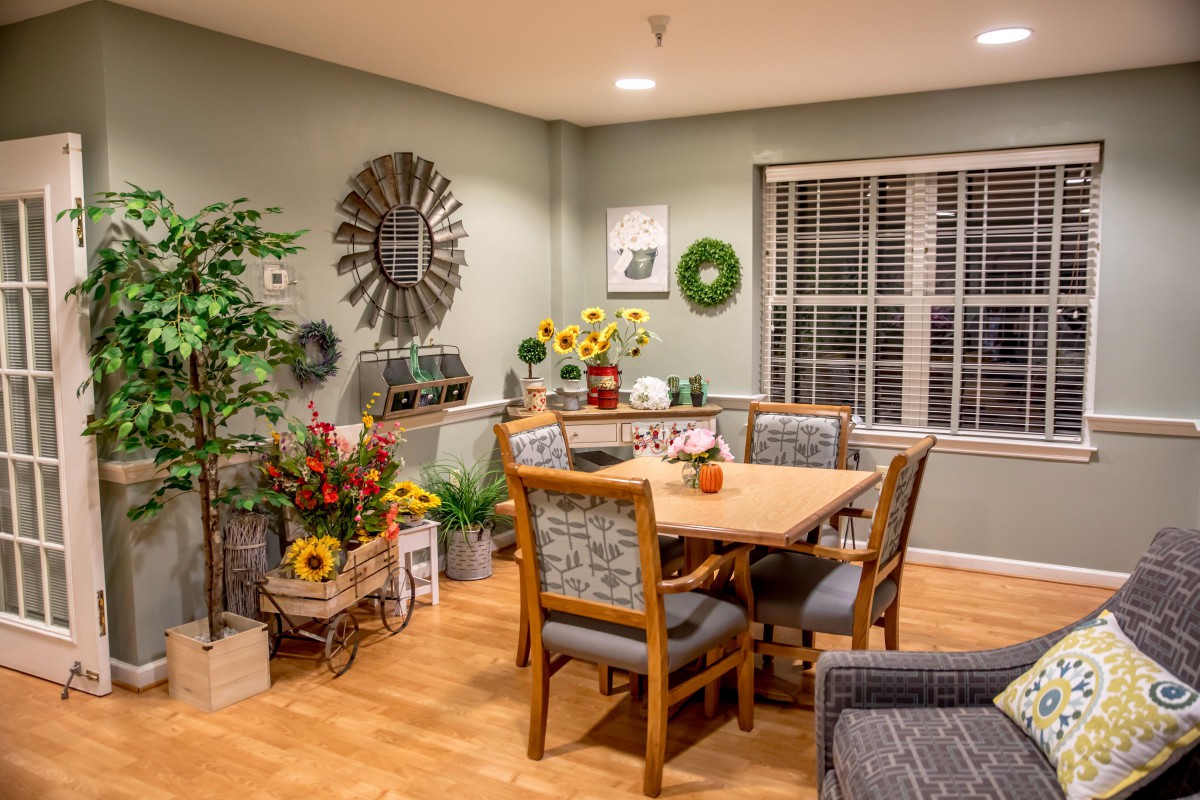 A cozy dining room with a wooden table and chairs, decorated with plants and wall art.