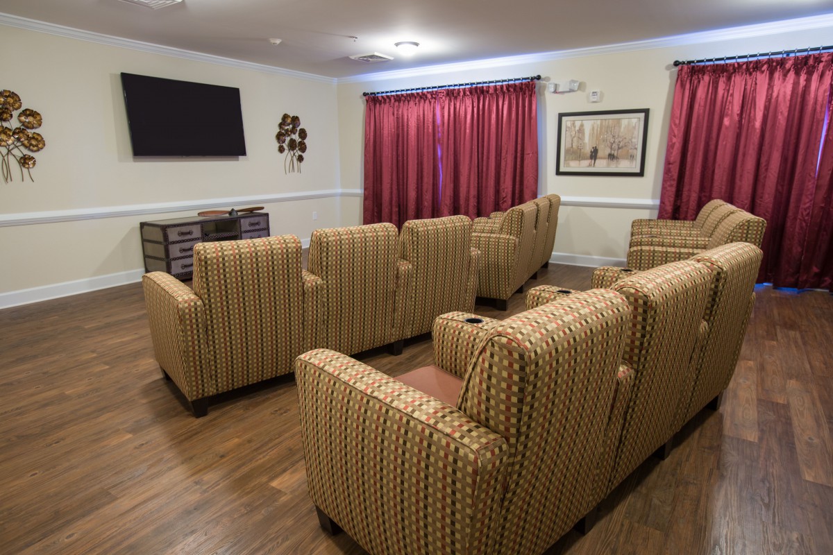 A cozy theater room with rows of comfortable chairs facing a large television, complemented by red curtains and warm lighting.