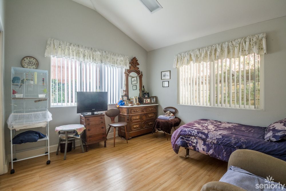 A cozy bedroom featuring a dresser with a mirror, a television, and hardwood flooring.