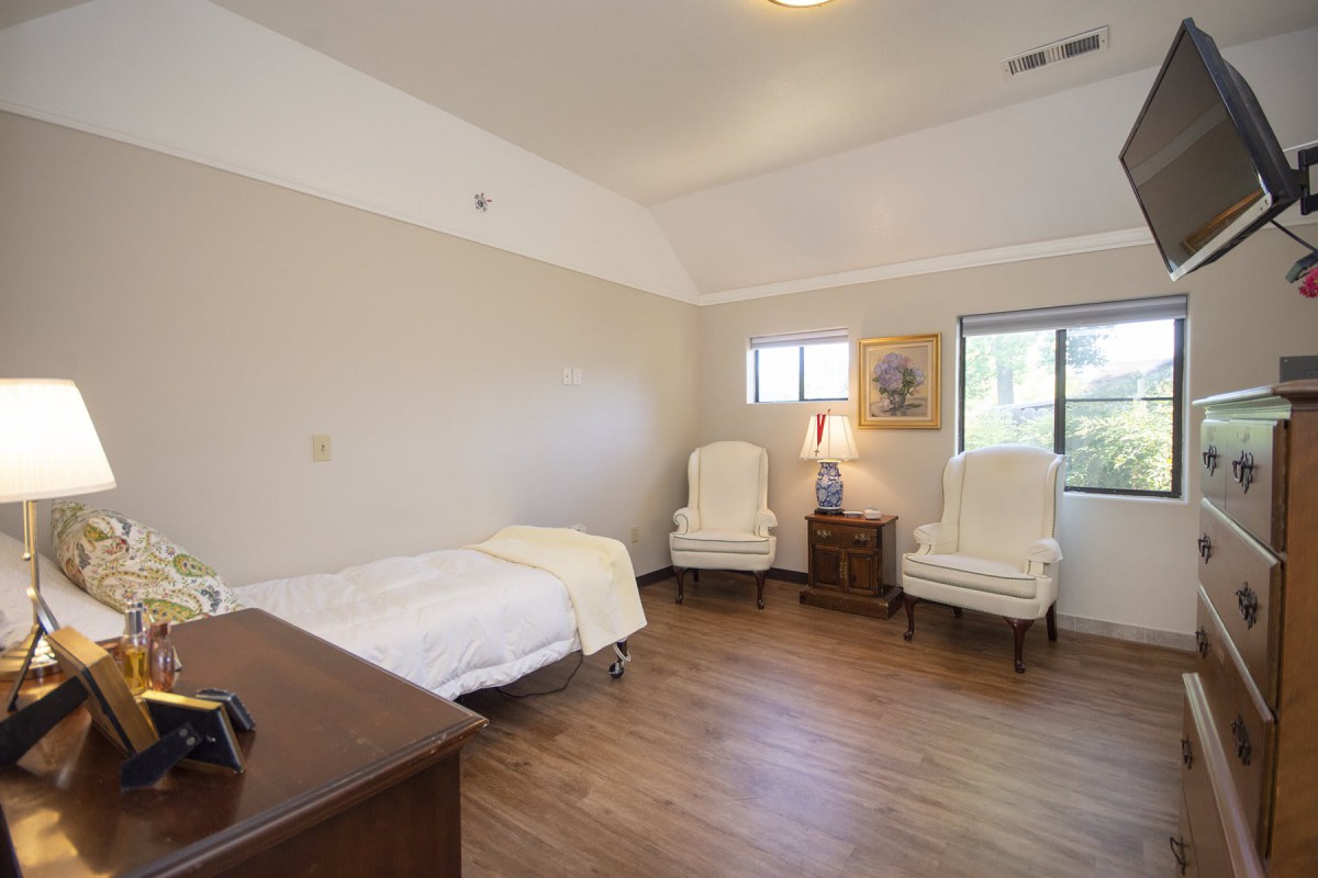 A minimalist bedroom with a single bed, two white chairs, and wooden flooring.