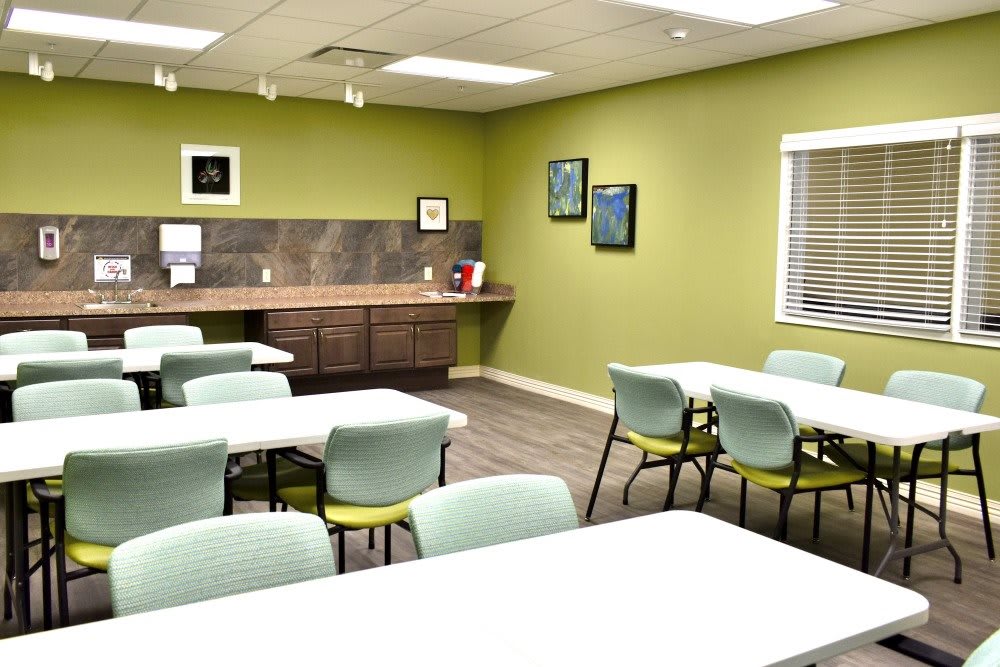 A modern classroom or meeting room with green walls, featuring tables and chairs arranged for group activities.