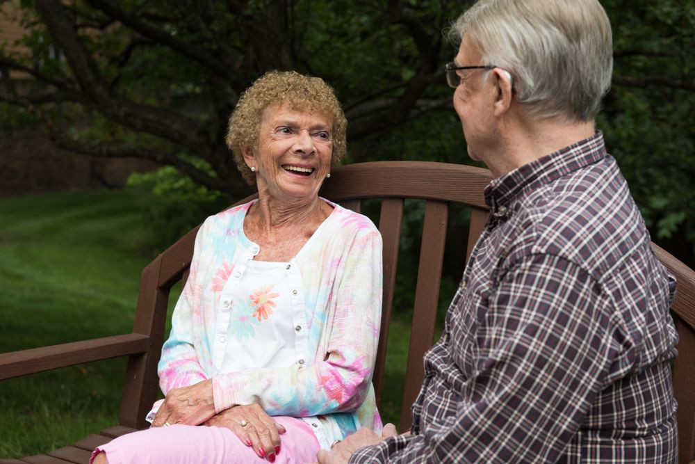 An elderly couple sitting on a park bench, engaged in a cheerful conversation.