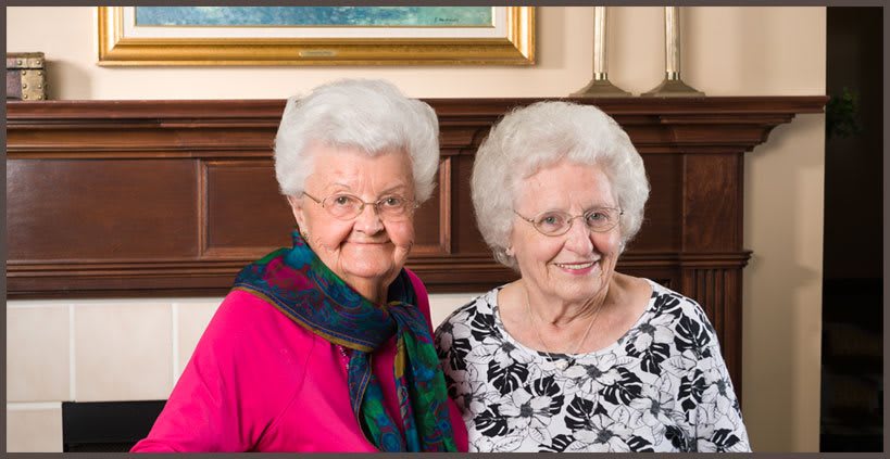 Two elderly women smiling together indoors.