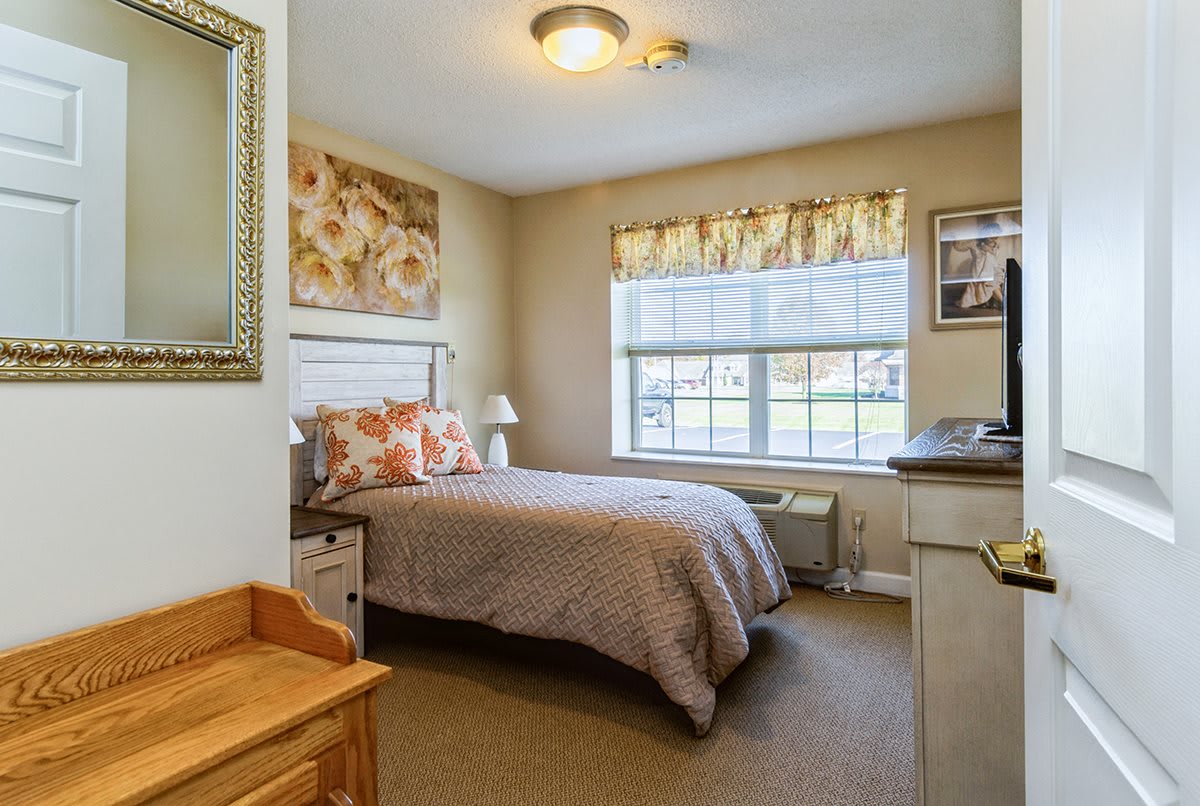 A cozy bedroom with a single bed, floral decor, and a large window allowing natural light.