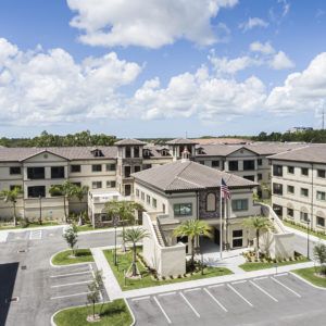 Aerial view of a large building complex with a parking lot and landscaped surroundings under a partly cloudy sky.