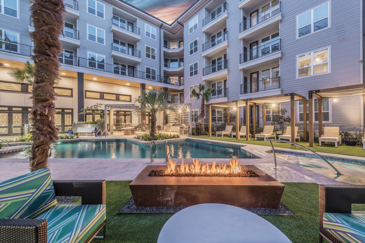 Modern apartment complex with a pool and fire pit in the evening.
