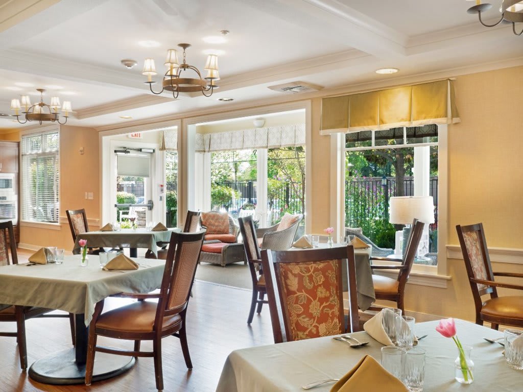 A well-lit dining area with neatly arranged tables and chairs, featuring large windows that provide natural light and a view of the outdoors.