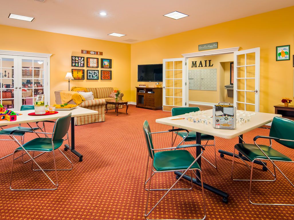 A cozy lounge area with tables, chairs, a couch, and a television, featuring yellow walls and vibrant decor.