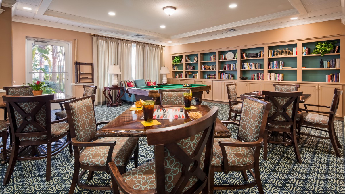 A cozy game room with a pool table, surrounded by bookshelves and comfortable seating.