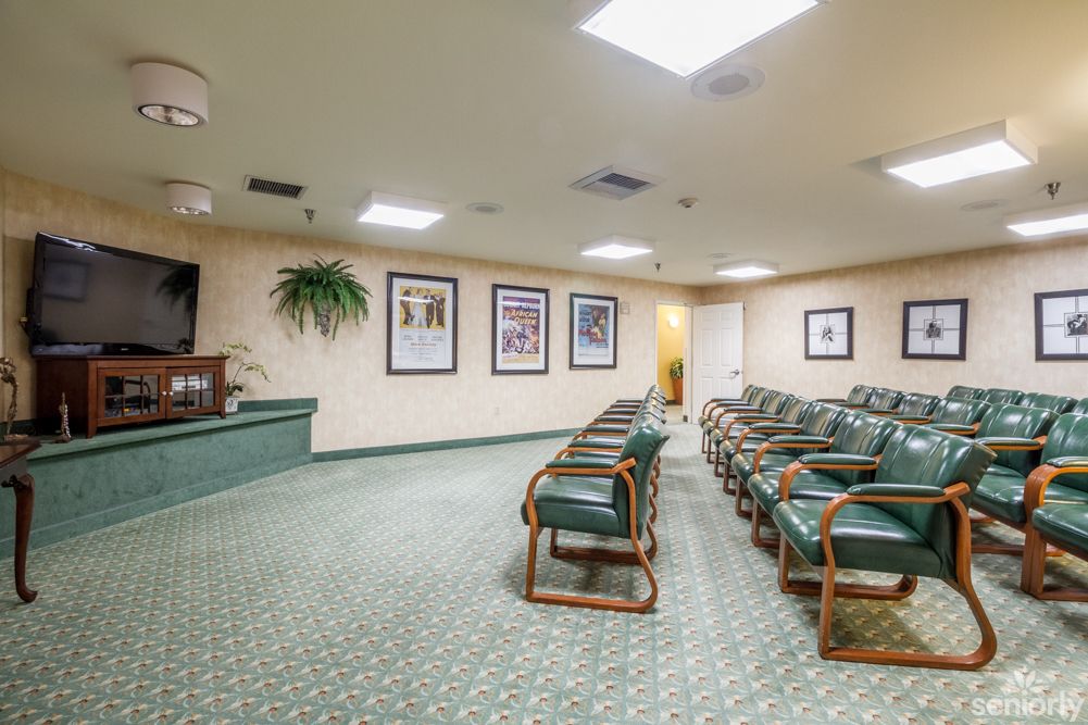 An empty waiting room with green chairs and carpet, adorned with framed pictures on the walls.