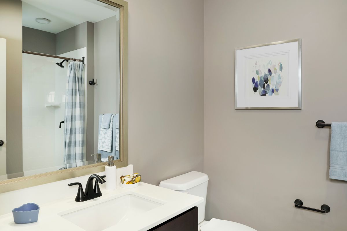 Modern bathroom featuring a sink with black fixtures, framed mirror, toilet, and abstract wall art.