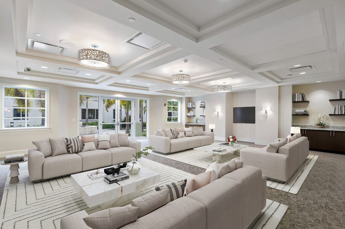 A spacious and modern living room with neutral tones, featuring multiple sofas, a coffered ceiling, and elegant decor.