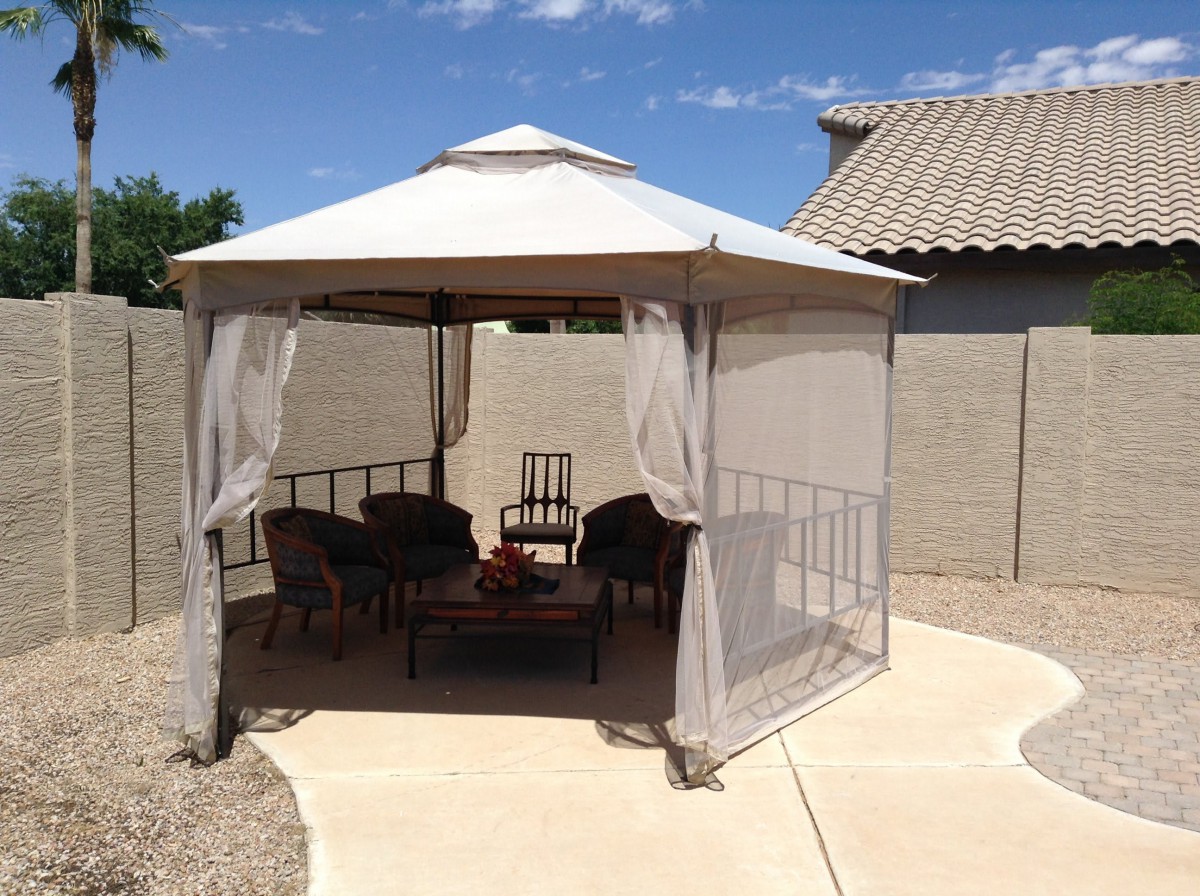 A cozy gazebo setup with chairs and a table in a sunny backyard.