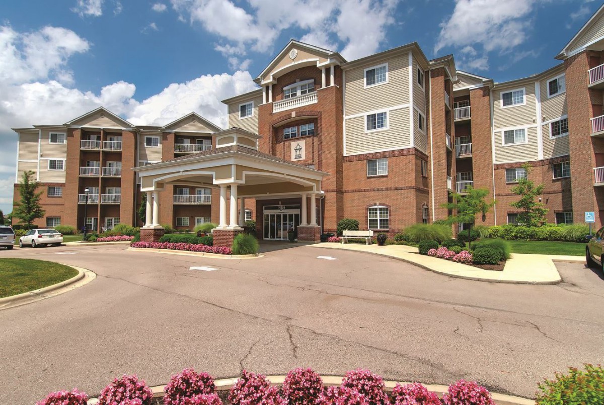 A multi-story hotel building with an entrance surrounded by landscaping under a partly cloudy sky.