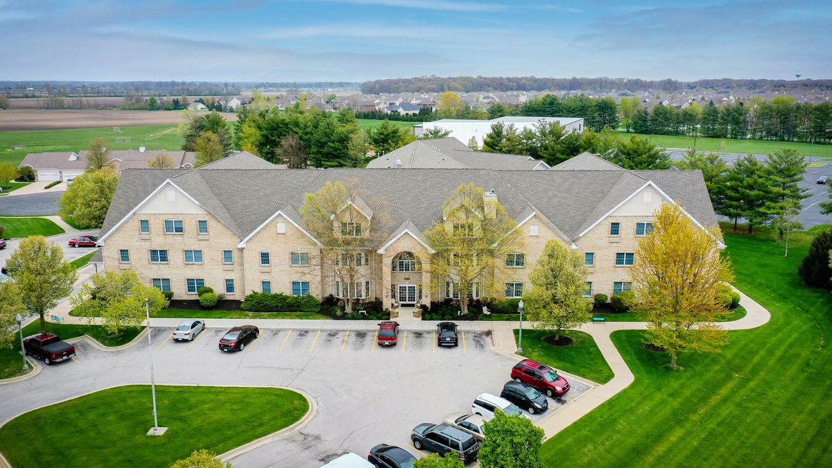 Aerial view of a large building with a parking lot and surrounding greenery.