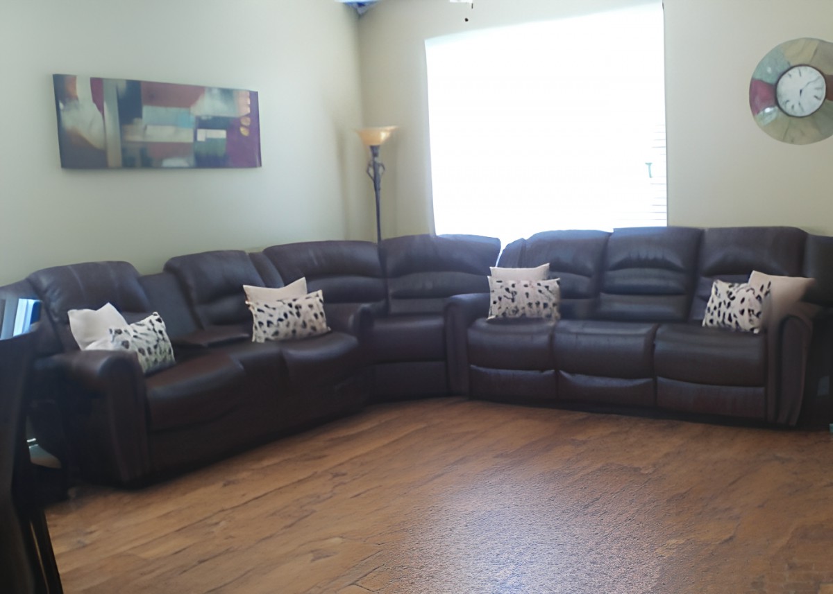 A cozy living room featuring a large dark leather sectional sofa adorned with decorative pillows, complemented by a floor lamp and wooden flooring.