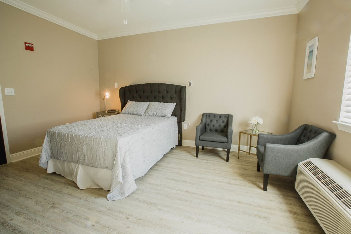 A modern, minimalist bedroom with a bed and two chairs.
