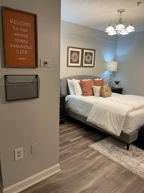 A cozy and modern bedroom featuring a neatly made bed, decorative pillows, wall art, and a bedside lamp.