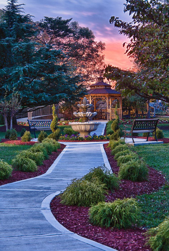 A beautiful garden pathway leading to a gazebo, surrounded by lush greenery and a stunning sunset sky.