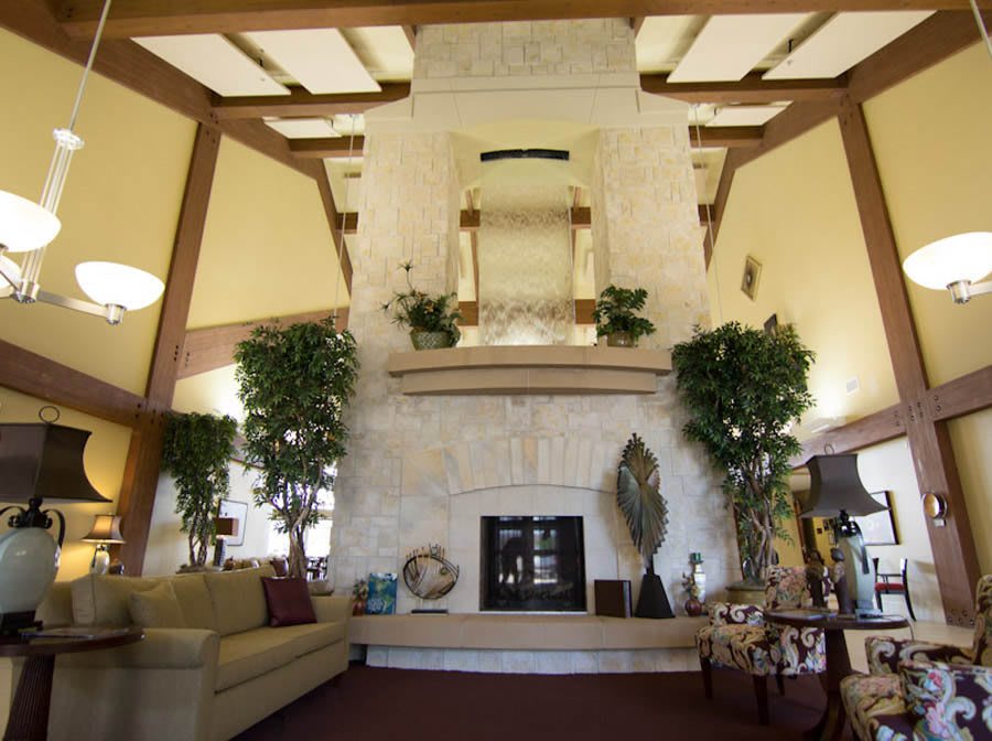 A spacious living room featuring a tall, central fireplace surrounded by plants and modern furnishings.
