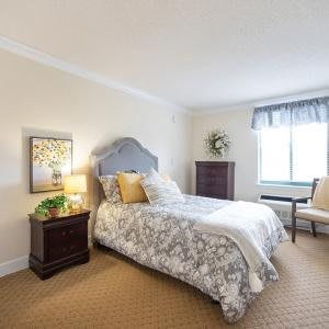 A cozy bedroom with a single bed, neatly arranged furniture, and soft lighting from a lamp on the nightstand.