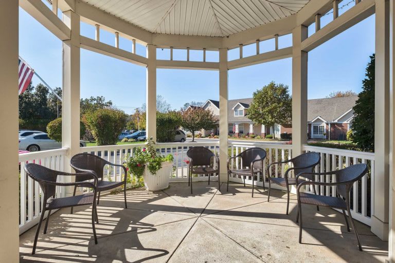 A cozy gazebo with several chairs overlooks a quiet neighborhood street.
