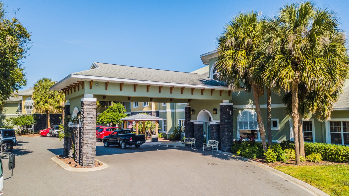 The entrance of a hotel with palm trees and a driveway under a clear blue sky.