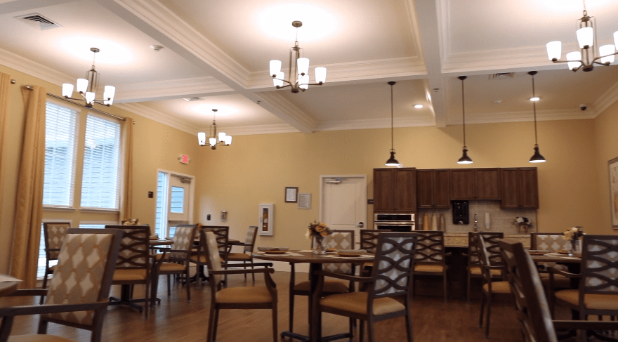 A cozy dining area with tables and chairs, featuring elegant lighting and a small kitchen section.
