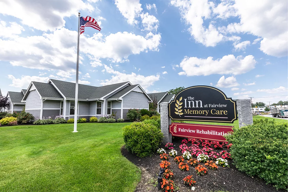 A care facility with an American flag and well-maintained landscaping under a partly cloudy sky.