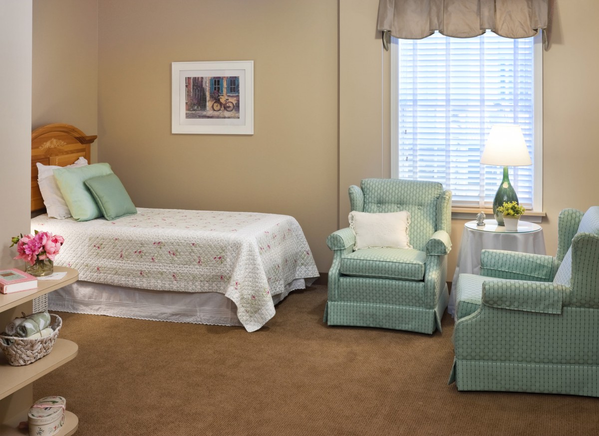 A cozy bedroom with a single bed, armchairs, and a window letting in natural light.