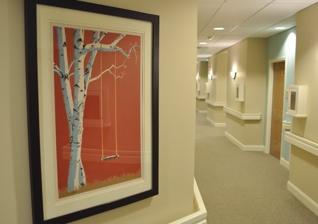 A hallway with a framed painting of a tree and swing on the wall.