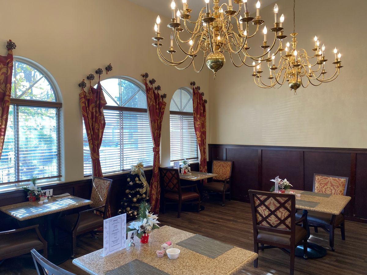 A cozy restaurant interior featuring elegant chandeliers and neatly arranged dining tables by large windows.