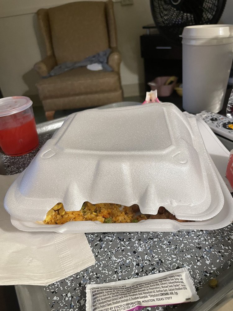 A styrofoam takeout container on a table with some food peeking out.