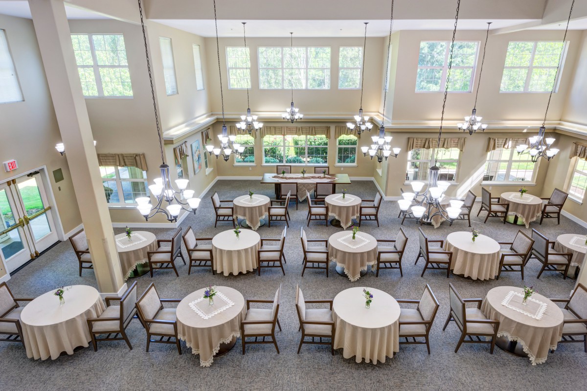 A spacious and elegant dining hall with round tables, chairs, and chandeliers.