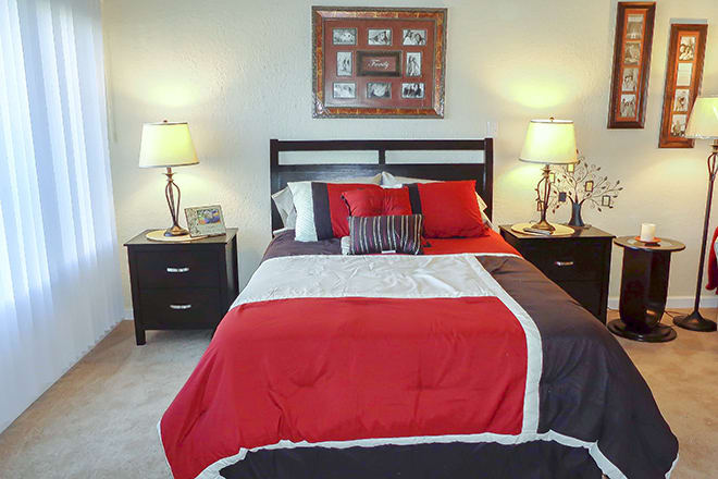 A neatly arranged bedroom with a red, white, and black color scheme, featuring a bed flanked by two lamps on nightstands.