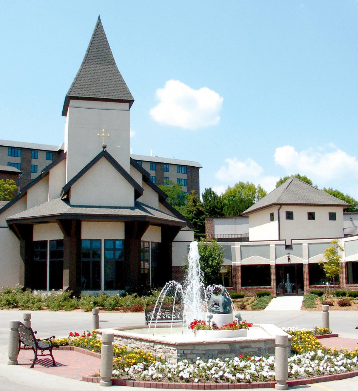 A picturesque building with a tower and a fountain in the foreground, surrounded by a garden and flowers.