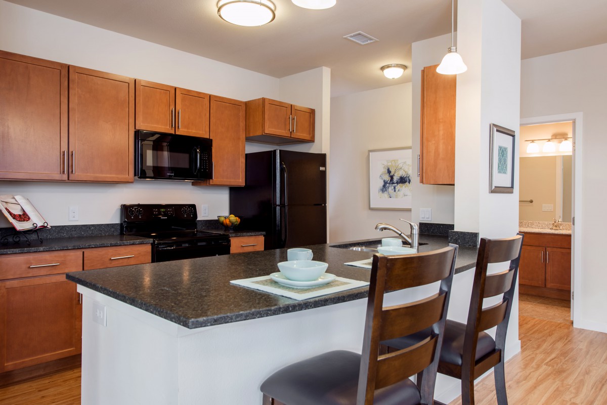 A modern kitchen with wooden cabinets, appliances, and a dining area featuring bar stools at the counter.