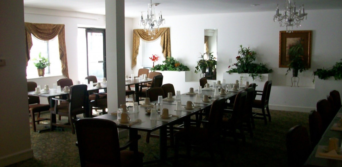A spacious dining area with elegantly set tables, adorned with a chandelier and decorative plants.