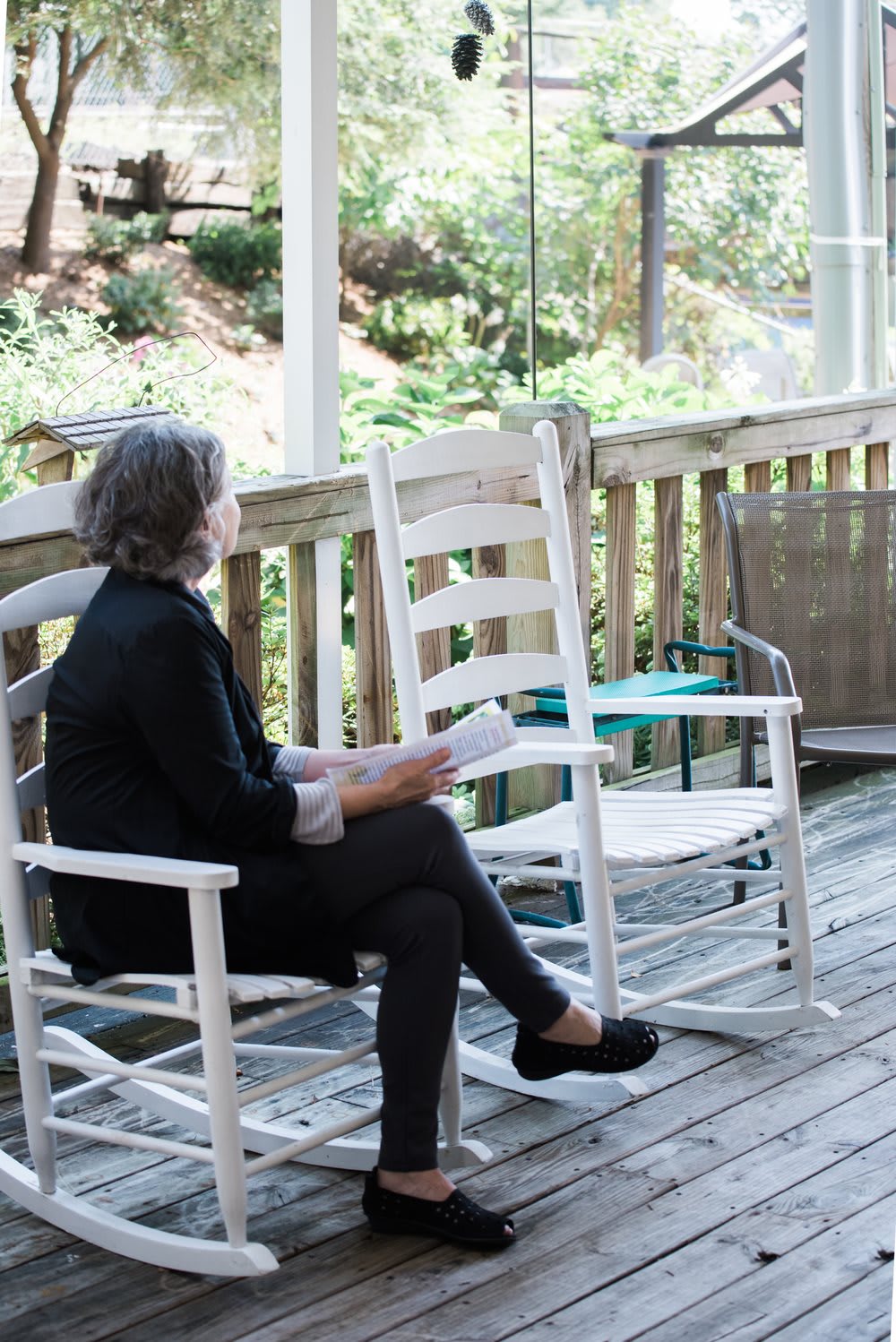 A woman sits on a wooden deck in a rocking chair, reading and enjoying the outdoors.