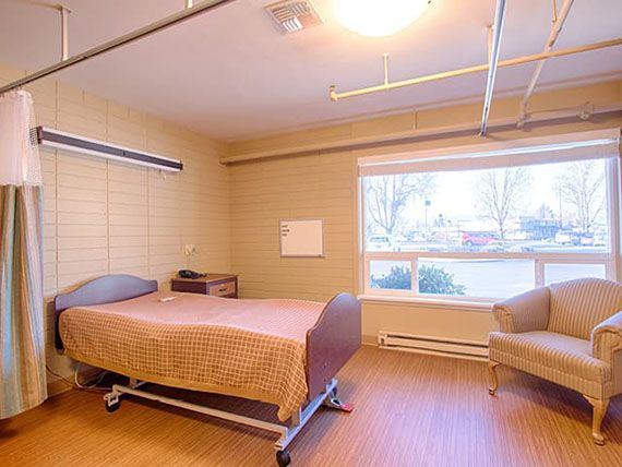 A hospital room with a single bed, large window, and minimal furniture.