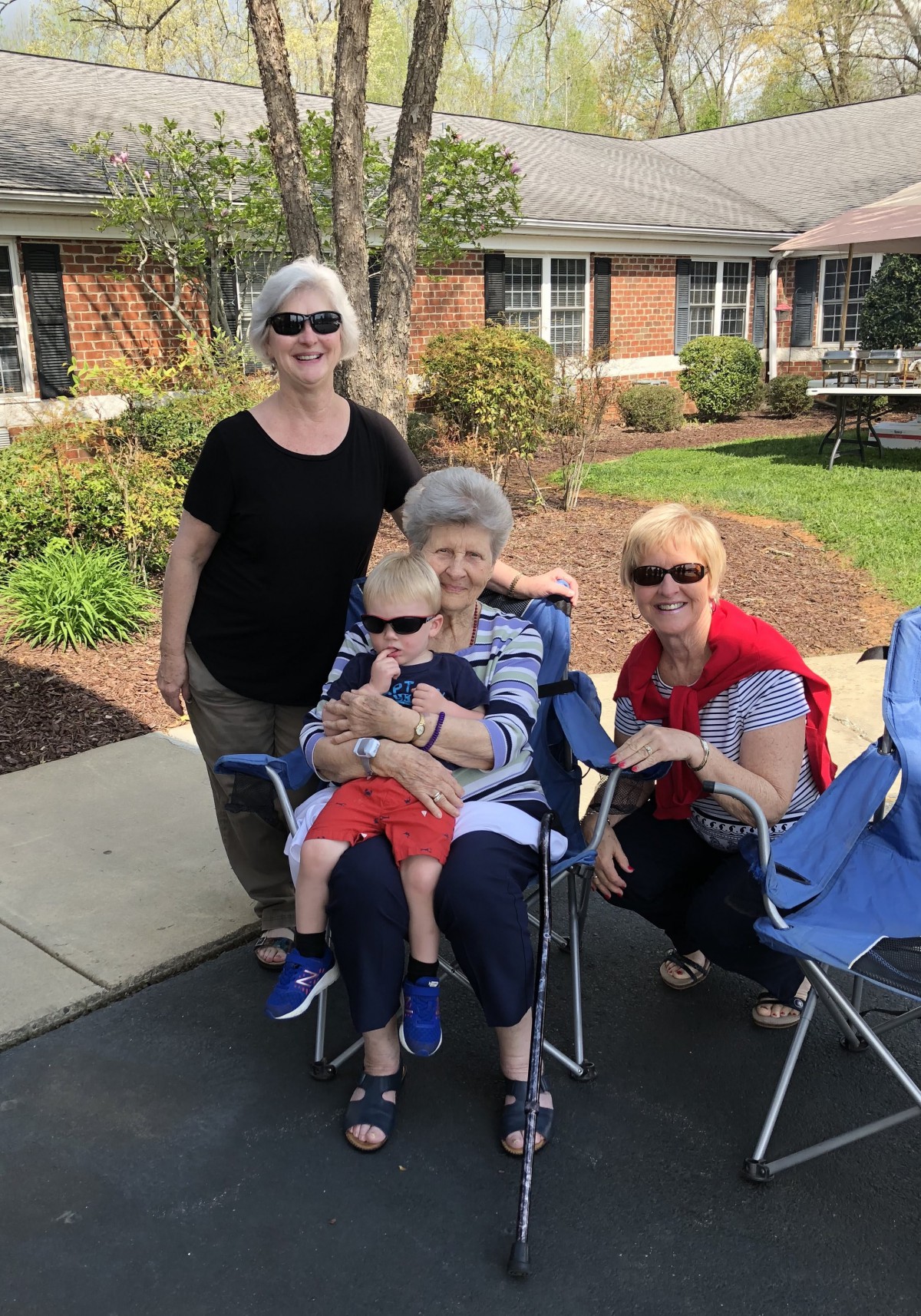 A family gathering outdoors with three adults and a child sitting on chairs.