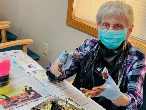 A senior person wearing a mask is engaging in a painting activity indoors.