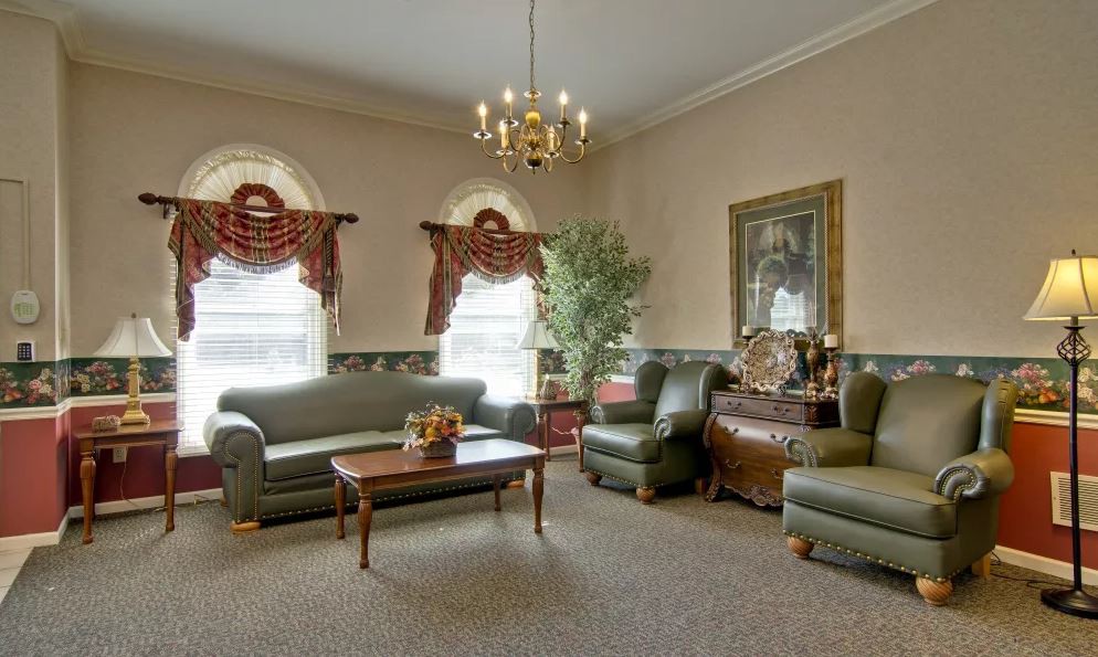 A traditional living room with elegant furnishings, including green sofas and armchairs, a wooden coffee table, decorative drapes, and a chandelier.