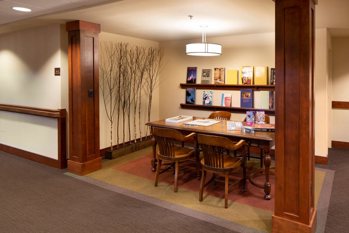 A cozy library reading area with a wooden table, chairs, and a bookshelf filled with books.