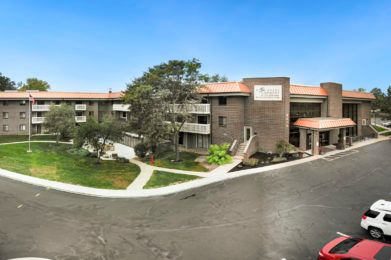 A modern residential apartment complex with well-maintained landscaping and clear blue skies.