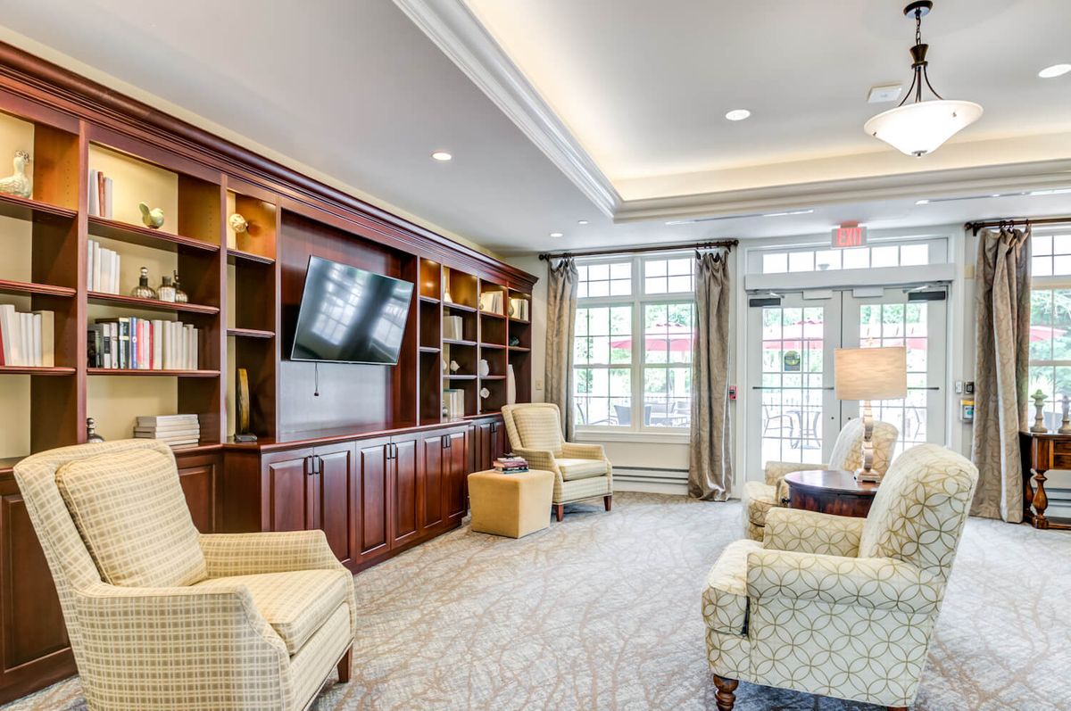 A cozy living room featuring armchairs, a large television on built-in bookshelves, and large windows allowing natural light to fill the space.