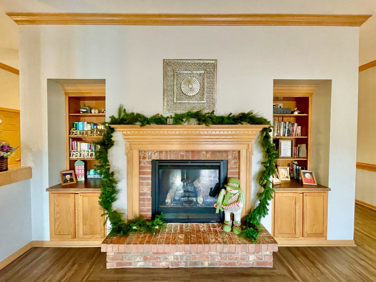 A cozy fireplace adorned with garland and ornaments, flanked by wooden bookshelves filled with books.